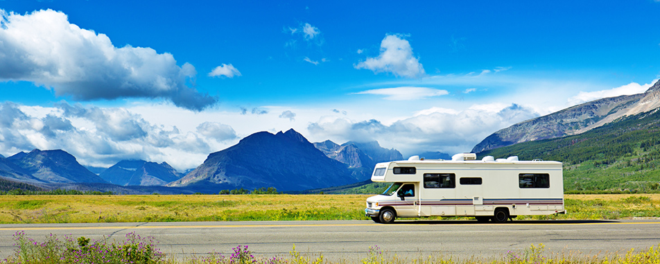 White motorhome RV driving on a highway with mountains and blue sky in the background White motorhome RV driving on a highway with mountains and blue sky in the background