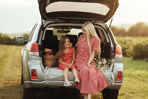 Woman and young girl wearing matching red and white polka dot dresses sitting at the open trunk of an SUV with a picnic basket and flowers