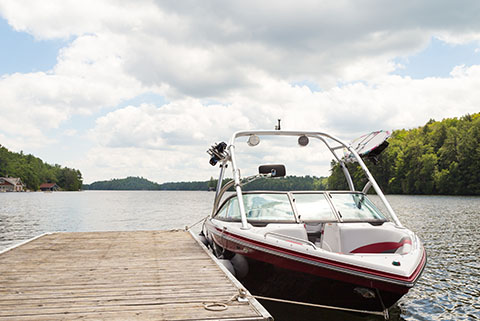 Speedboat docked at a wooden pier on a calm lake with trees and cloudy sky in the background Speedboat docked at a wooden pier on a calm lake with trees and cloudy sky in the background