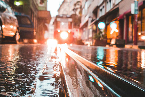 Wet tram tracks on a city street at dusk with a tram approaching in the background and reflections of lights on the wet surface