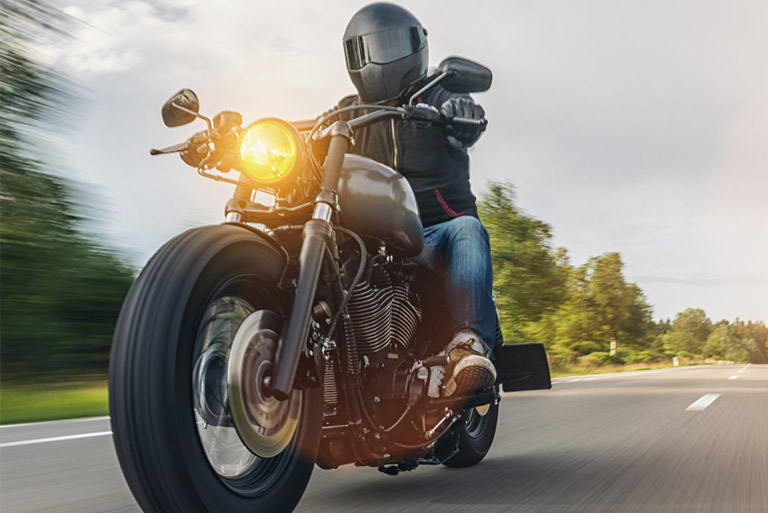 Motorcyclist wearing black helmet and jacket riding a black cruiser-style motorcycle on a country road at speed